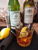 A French Kiss in a crystal glass in front of two bottles of vermouth