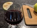 A deep red drink in a brandy snifter. An apple slice is balanced on the rim of the glass.