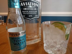 A gin and tonic beside a bottle of Aviation gin and Fever Tree Mediterranean tonic water