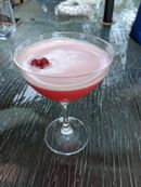 A vivid red cocktail topped with a white foam. A raspberry floats to one side atop the foam.