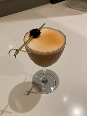 Cocktails with a frothy top, tinged brownish orange from the bitters. A cherry on a pick rests across the rim atop the foam.