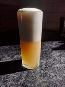 Narrow glass filled with a golden cocktail, the top half of which is white froth